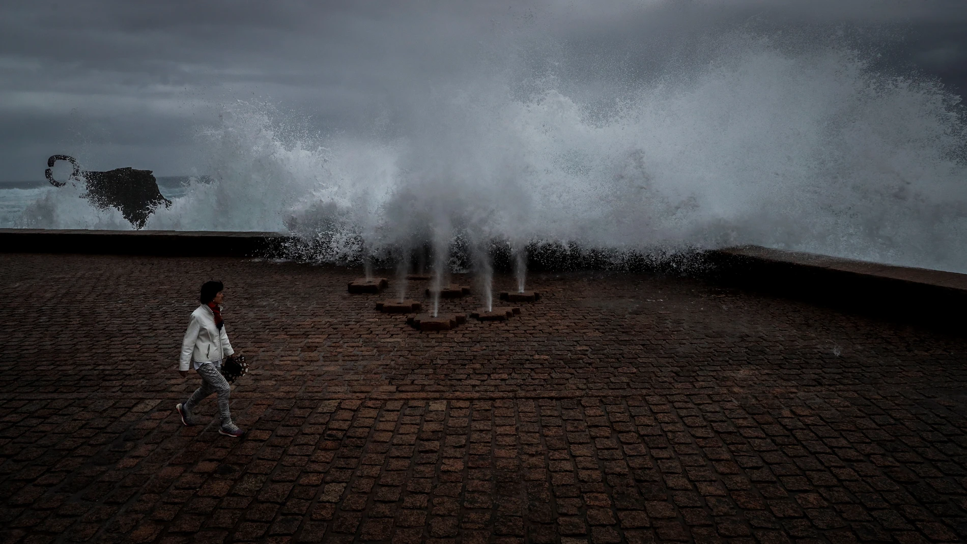 Una mujer pasea en San Sebastián junto a la obra escultórica "El peine del Viento"