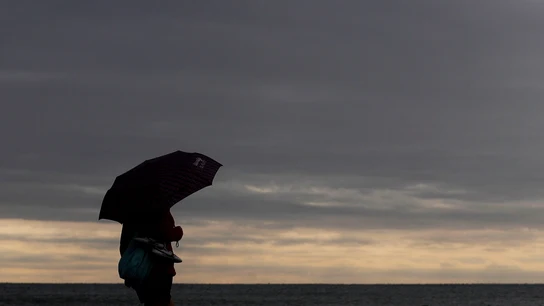 Una persona pasea por la playa de la Malvarrosa protegida con un paraguas Una persona pasea por la playa de la Malvarrosa protegida con un paraguas