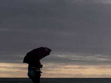 Una persona pasea por la playa de la Malvarrosa protegida con un paraguas Una persona pasea por la playa de la Malvarrosa protegida con un paraguas