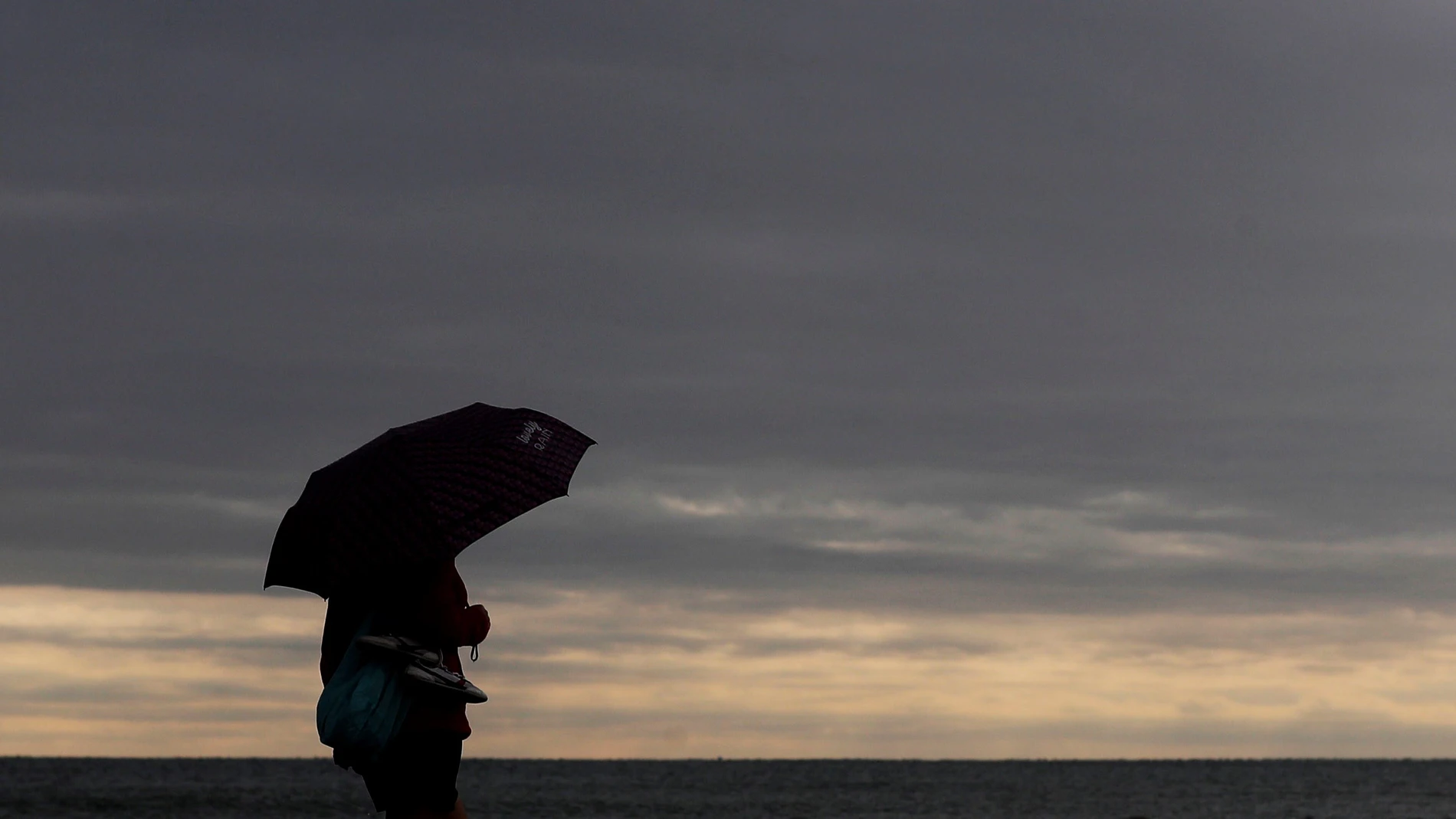 Una persona pasea por la playa de la Malvarrosa protegida con un paraguas