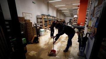  Varios empleados retiran agua y barro del interior de su comercio