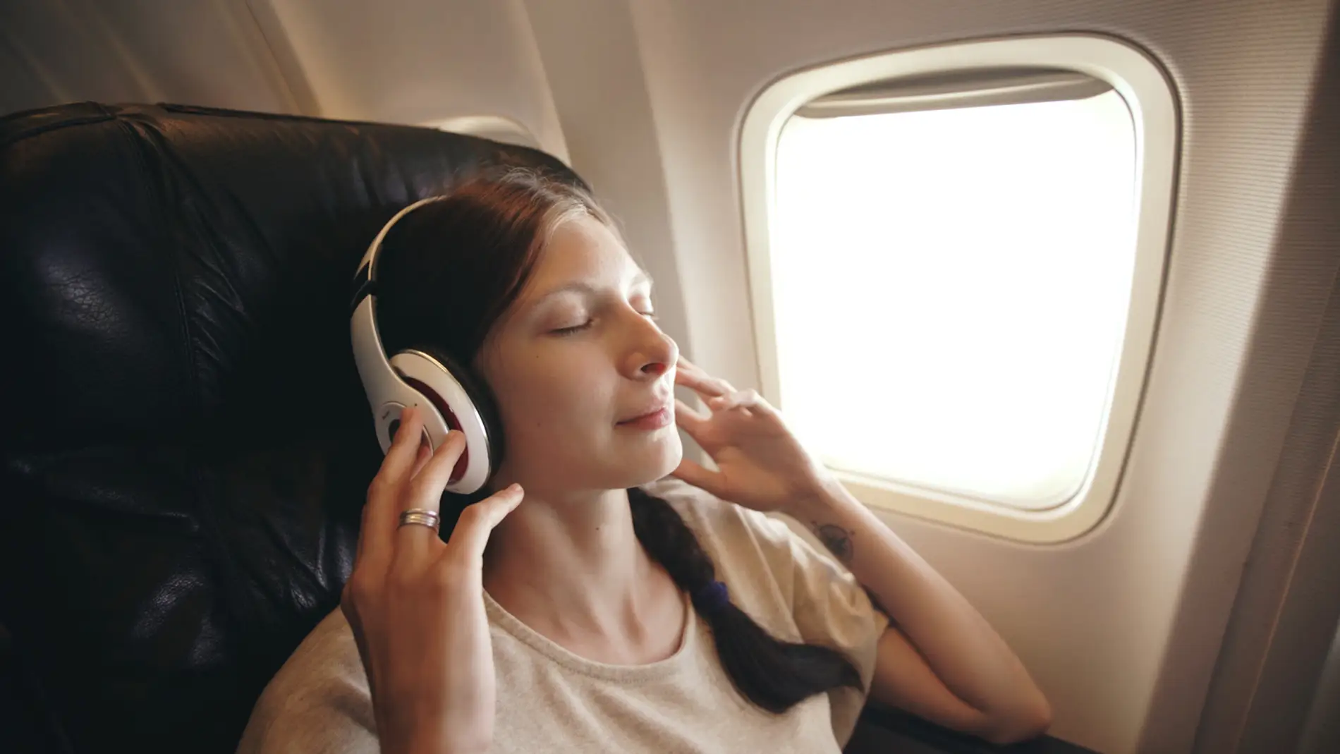 Joven escucha música con auriculares inalámbricos en el avión