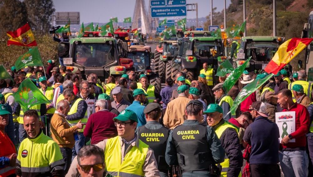 Agricultores junto a parte del más de un centenar de tractores y otros vehículos agrícolas durante el corte de tráfico en la autovía A-49corta la frontera con Portugal en Huelva