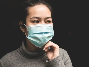 Una mujer con mascarilla tocándose la cara Una mujer con mascarilla tocándose la cara