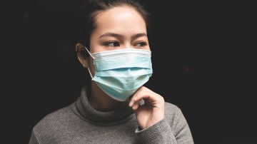 Una mujer con mascarilla tocándose la cara