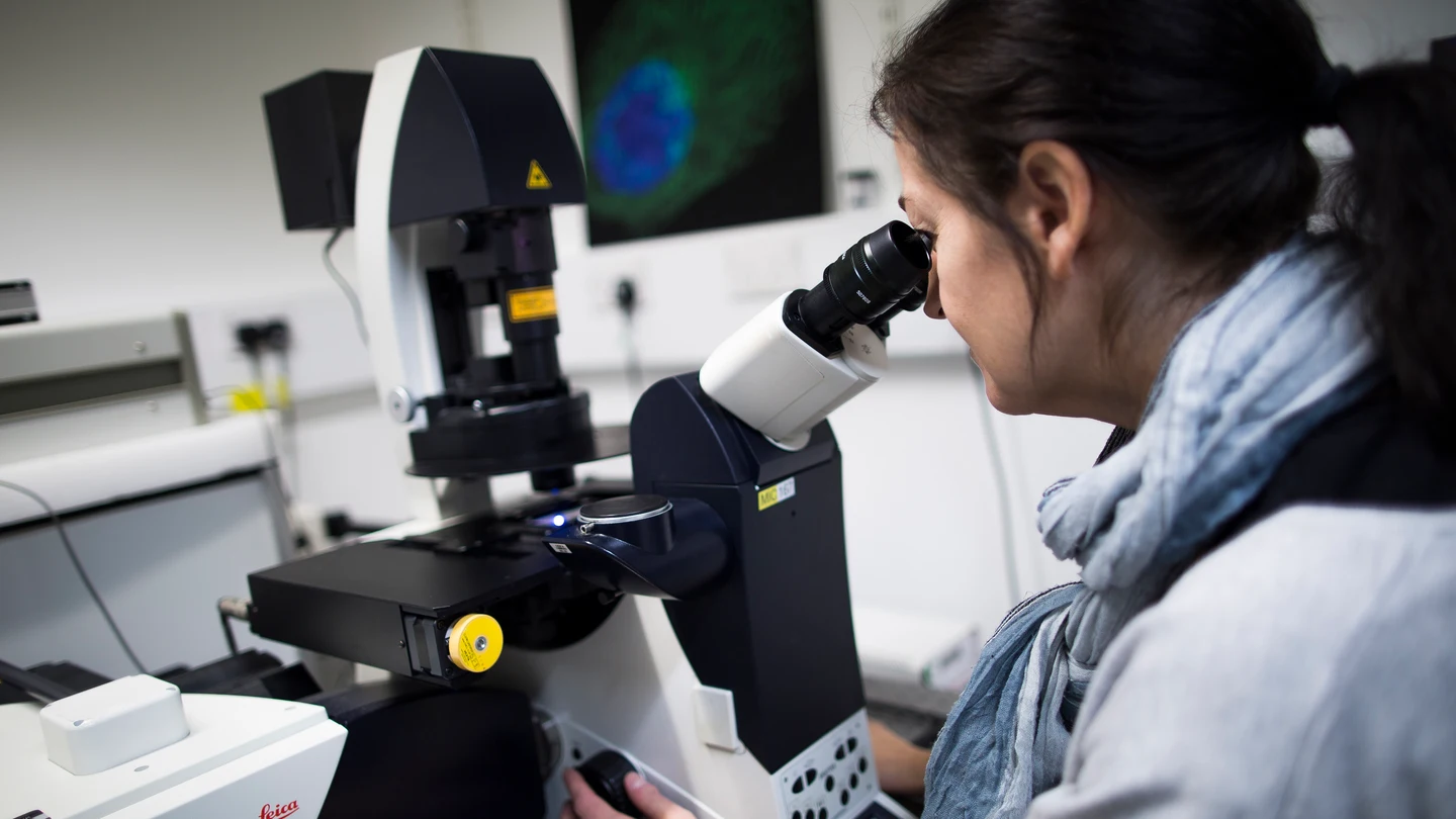 Una científica mira a través de un microscopio Una científica mira a través de un microscopio