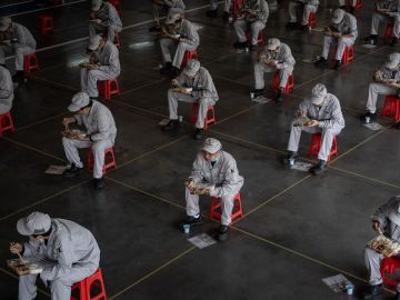 Trabajadores en una fábrica de Wuhan almuerzan guardando la distancia de seguridad por el coronavirus