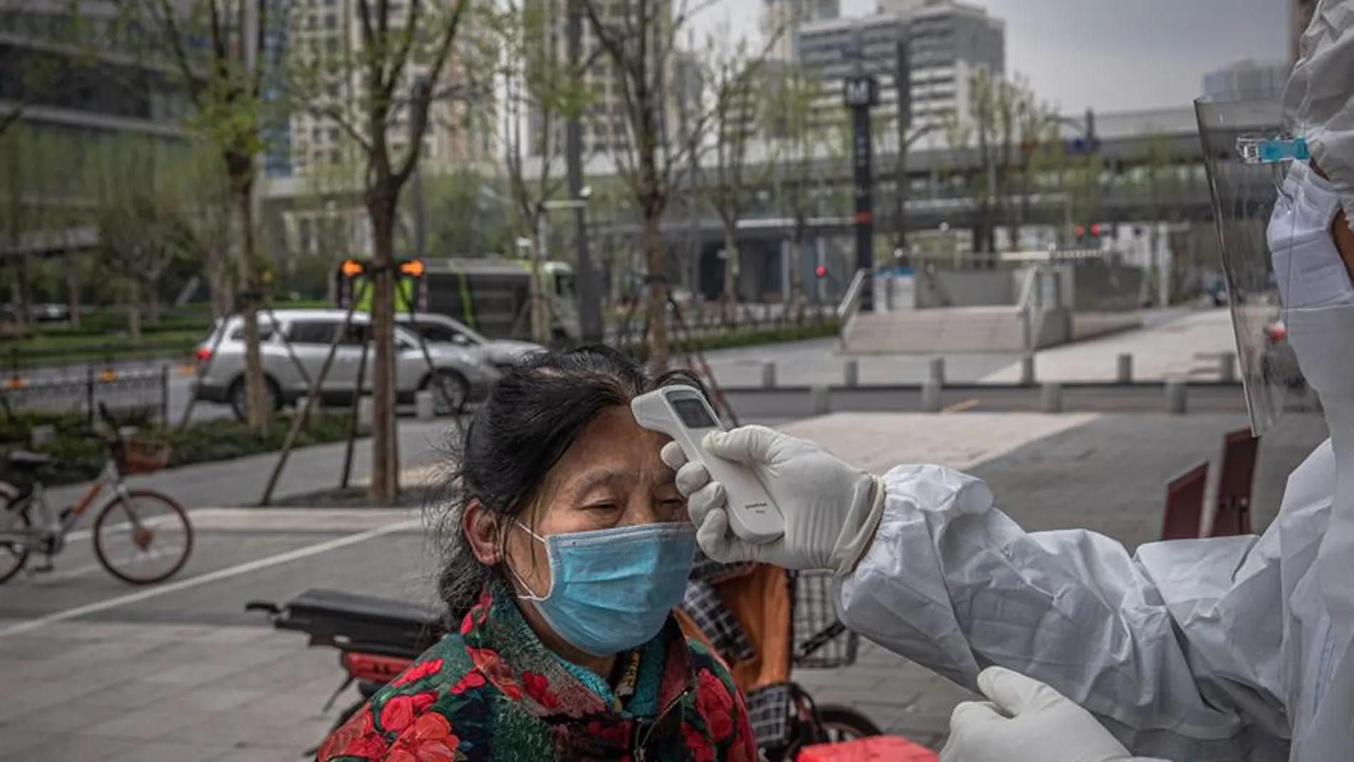 Un sanitario verifica la temperatura de una anciana a la entrada de un banco en Wuhan