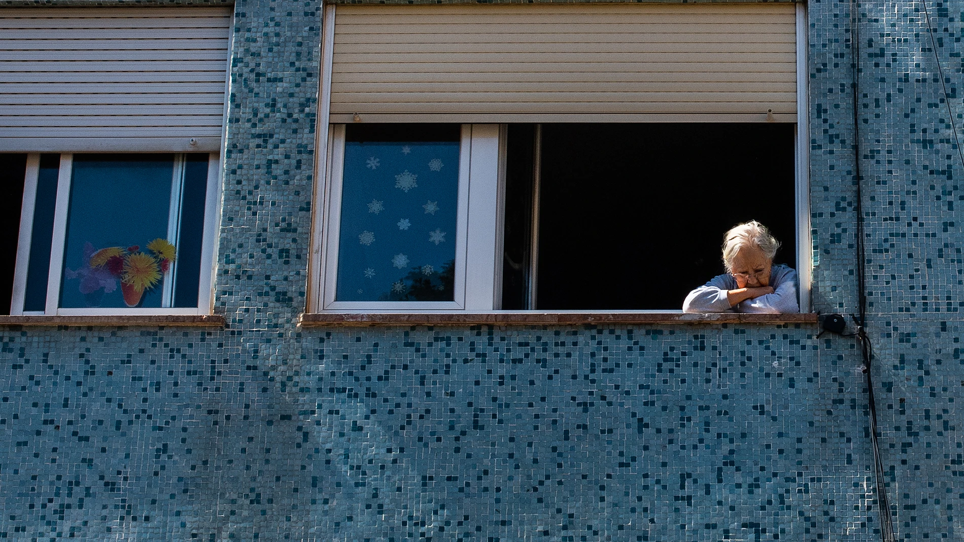 Una mujer mira a la calle por la ventana de su casa, en Barcelona