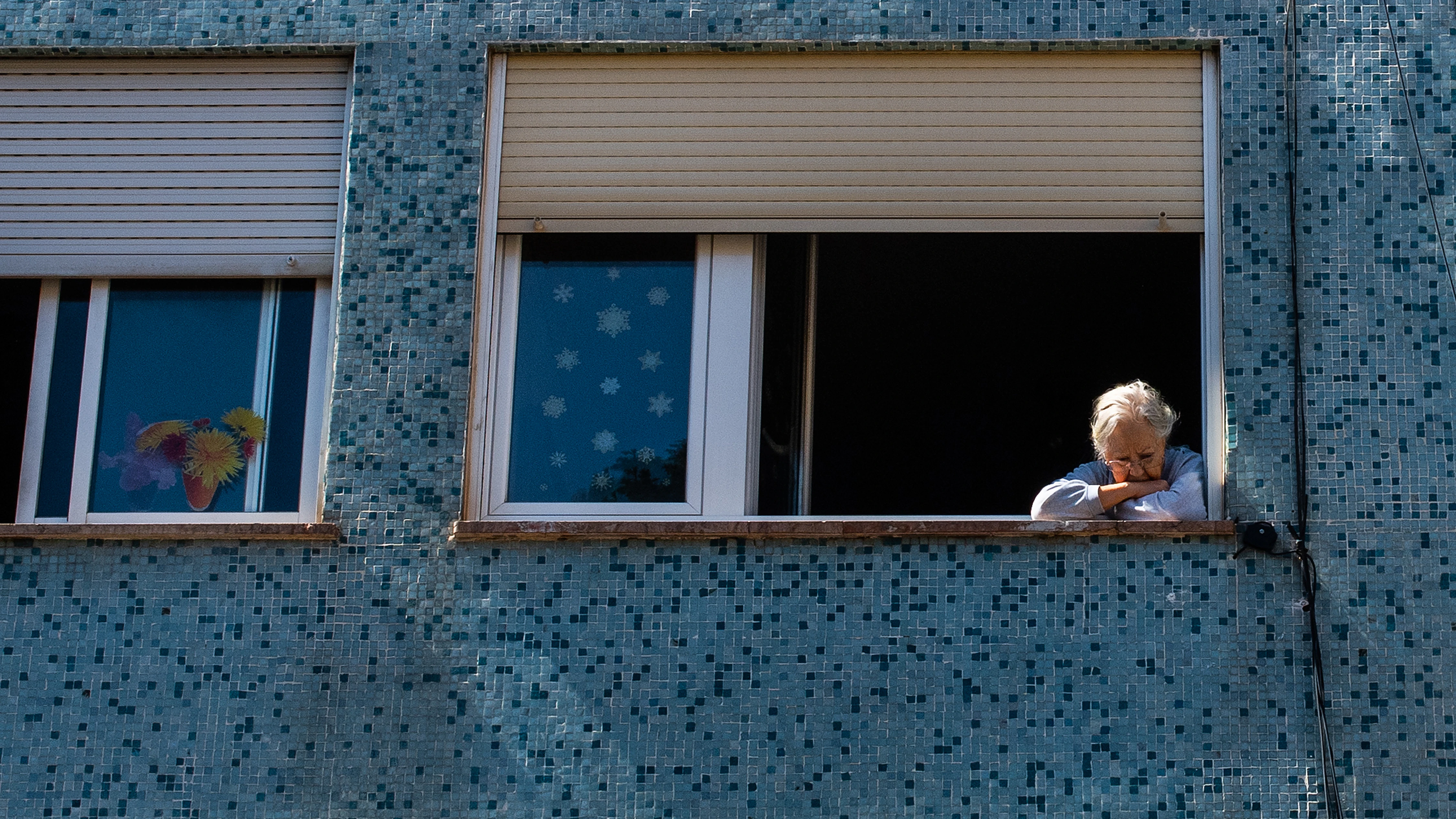 Una mujer mira a la calle por la ventana de su casa, en Barcelona