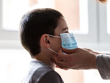 Una mujer coloca una mascarilla a un niño Una mujer coloca una mascarilla a un niño