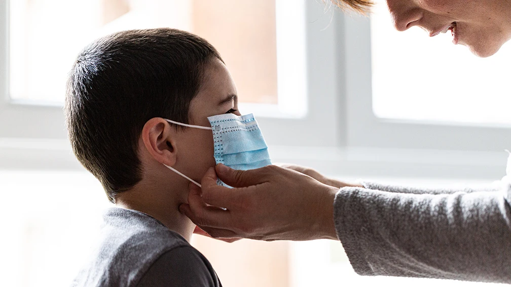 Una mujer coloca una mascarilla a un niño