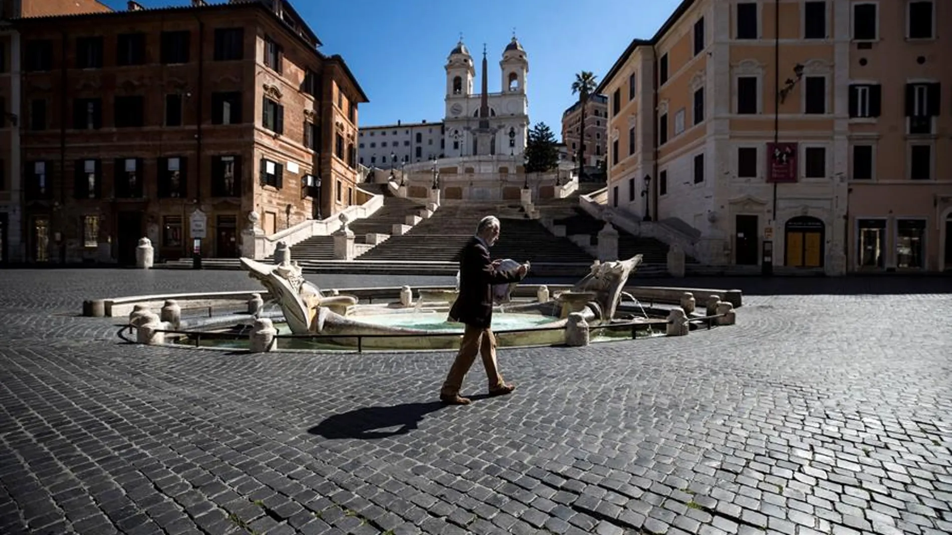 Una persona camina por la Piazza Spagna de Roma, desierta por el confinamiento por coronavirus