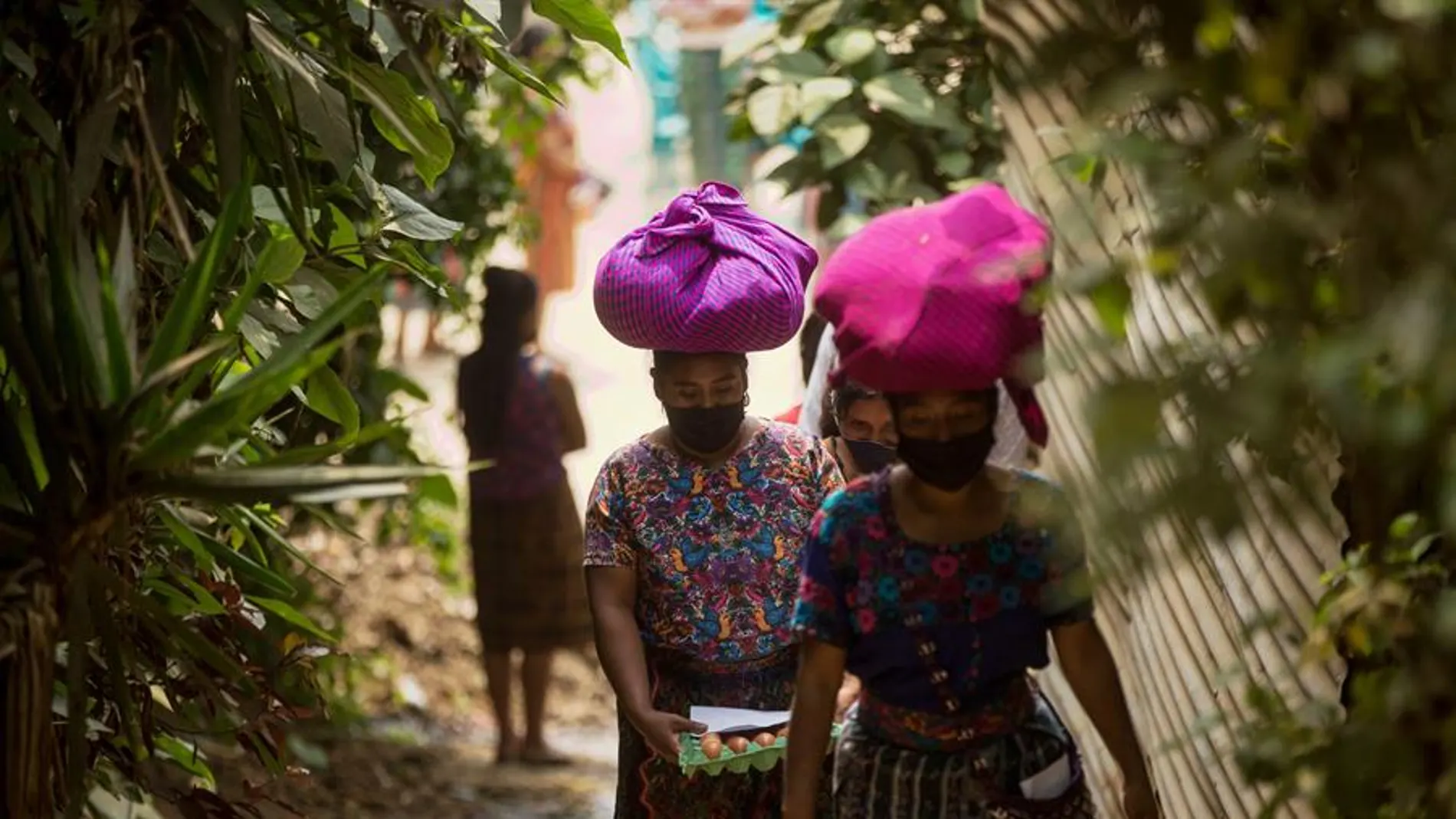 Mujeres con mascarilla portan alimentos entregados como ayuda alimentaria en Guatemala