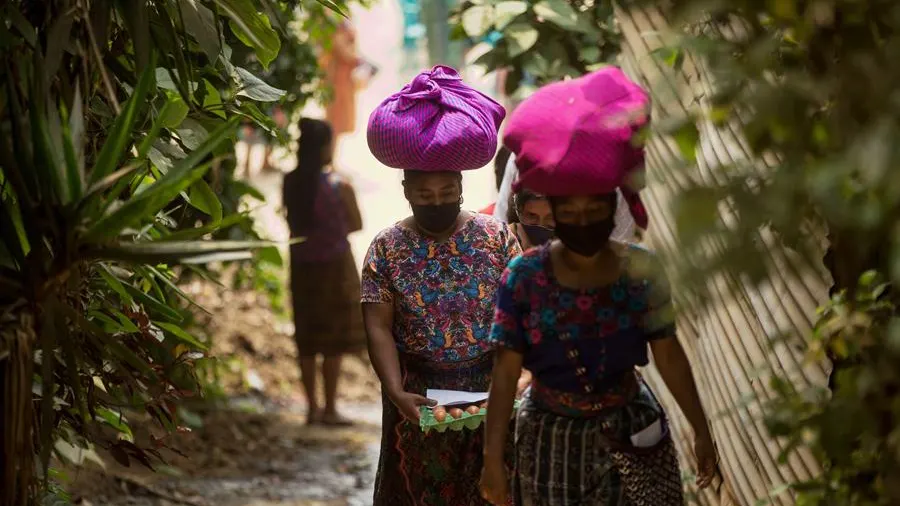 Mujeres con mascarilla portan alimentos entregados como ayuda alimentaria en Guatemala