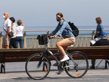 Una mujer pasea en bicicleta protegida con una mascarilla Una mujer pasea en bicicleta protegida con una mascarilla