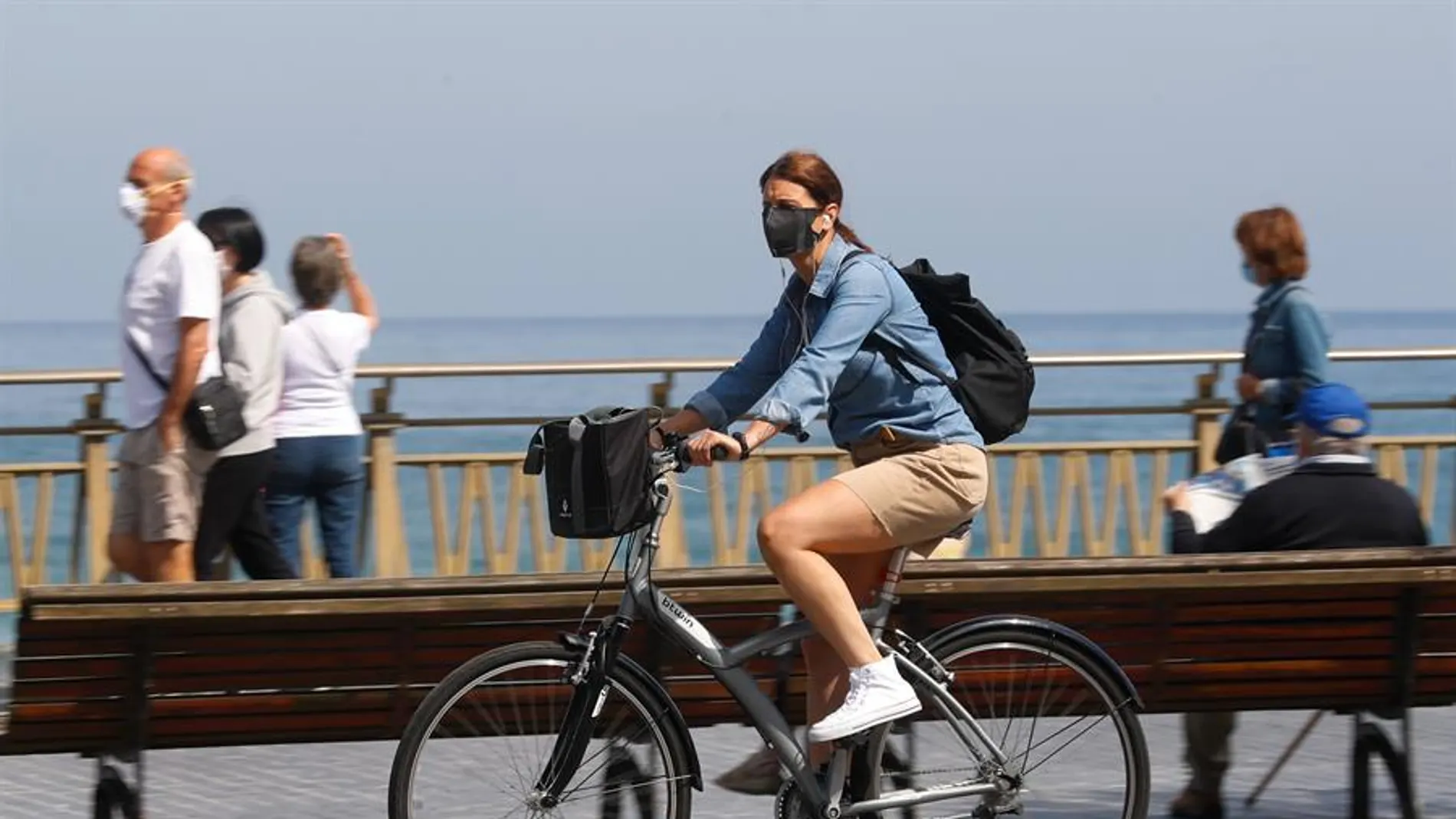 Una mujer pasea en bicicleta protegida con una mascarilla
