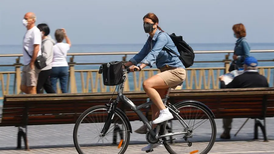 Una mujer pasea en bicicleta protegida con una mascarilla