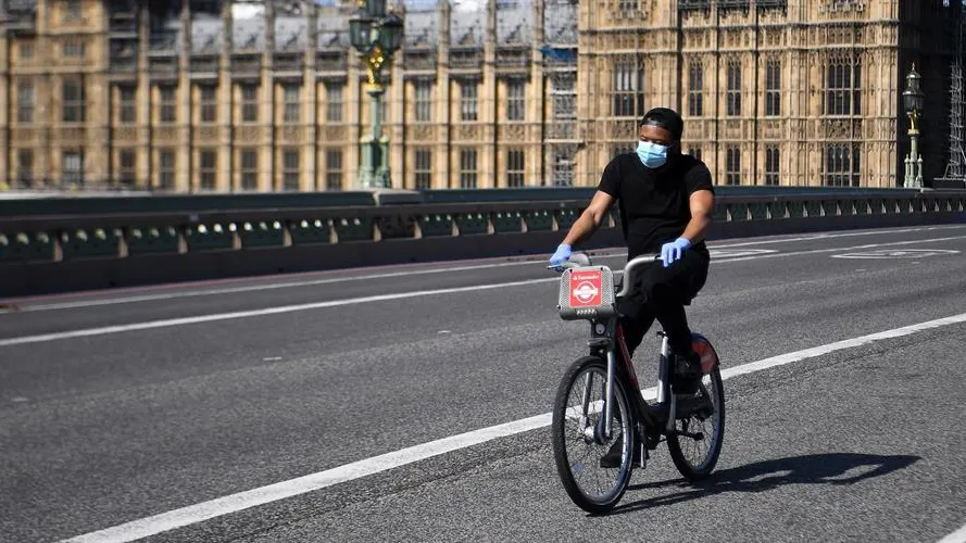 Un hombre con mascarilla circula en bicicleta frente al Parlamento británico en Londres