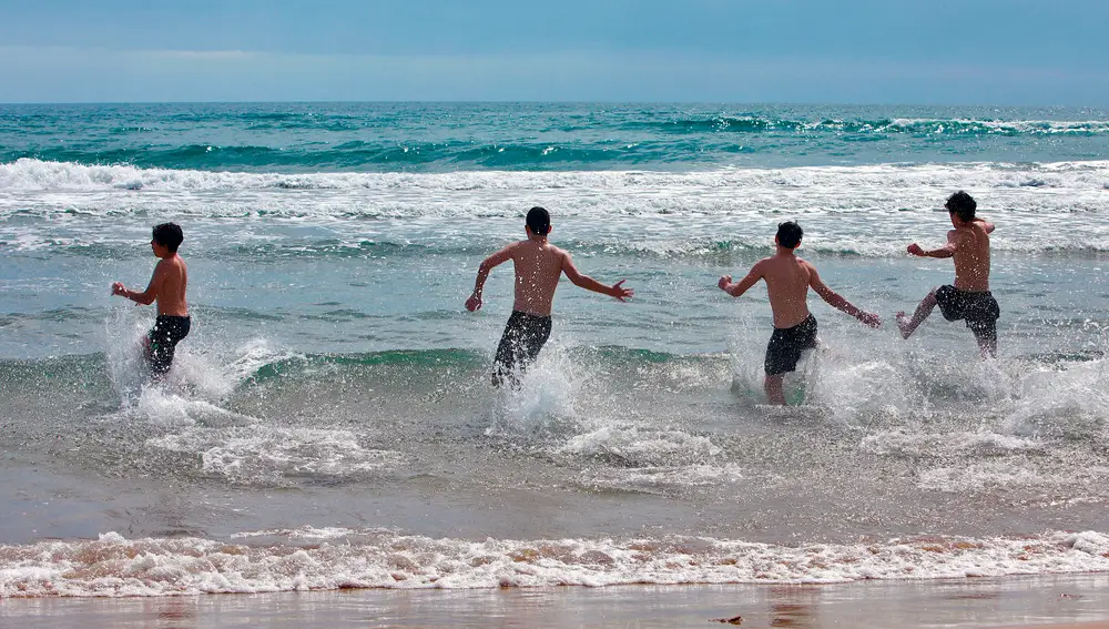  Varios jóvenes disfrutan del mar en la playa de Gandía