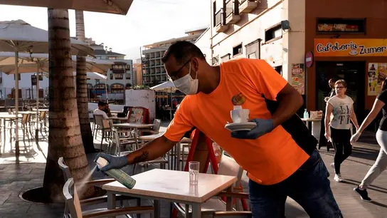 Un camarero desinfecta unas sillas de una terraza de un bar. Un camarero desinfecta unas sillas de una terraza de un bar.