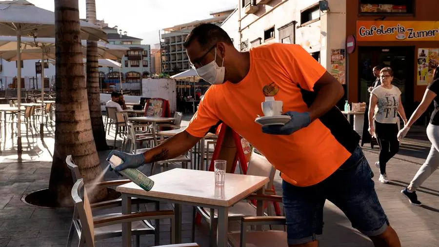 Un camarero desinfecta unas sillas de una terraza de un bar.