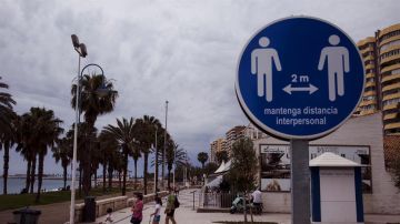 Una familia en el paseo marítimo de la Malagueta ante un disco que recuerda mantener la distancia de 2 metros entre personas