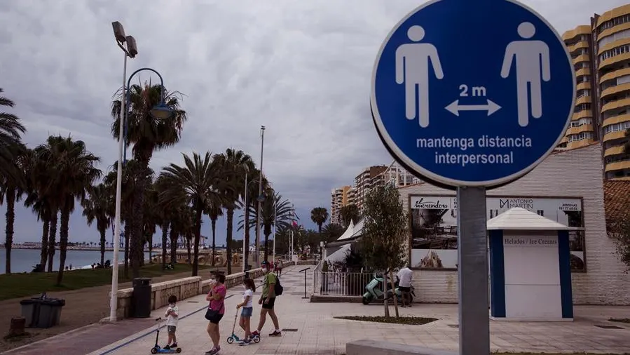 Una familia en el paseo marítimo de la Malagueta ante un disco que recuerda mantener la distancia de 2 metros entre personas