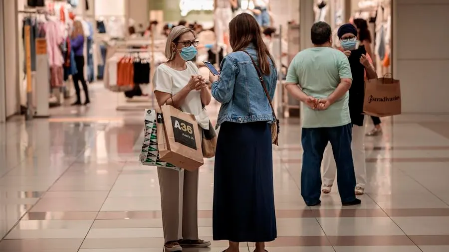 Varias personas realizan compras en un centro comercial con mascarillas.