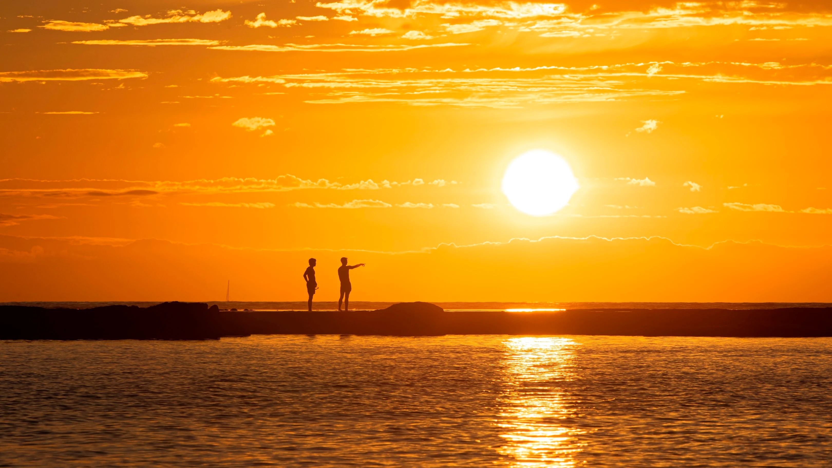 Unos bañistas contemplan el atardecer desde la barra natural de la playa de Las Canteras, en Las Palmas de Gran Canaria