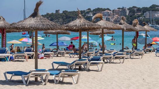 Imagen de unas sombrillas y hamacas vac&iacute;as en la arena en una playa