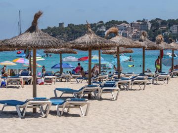Imagen de unas sombrillas y hamacas vacías en la arena en una playa Imagen de unas sombrillas y hamacas vacías en la arena en una playa