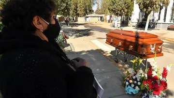 Una mujer espera junto a un féretro afuera del cementerio
