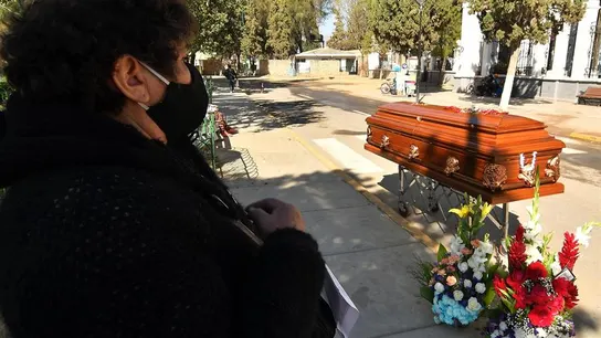 Una mujer espera junto a un féretro afuera del cementerio Una mujer espera junto a un féretro afuera del cementerio