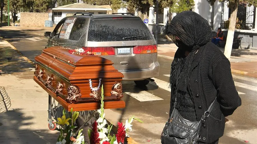 Una mujer espera junto a un féretro afuera de un cementerio