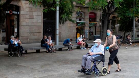Una mujer empuja la silla de un se&ntilde;or mayor en el centro de Barcelona.