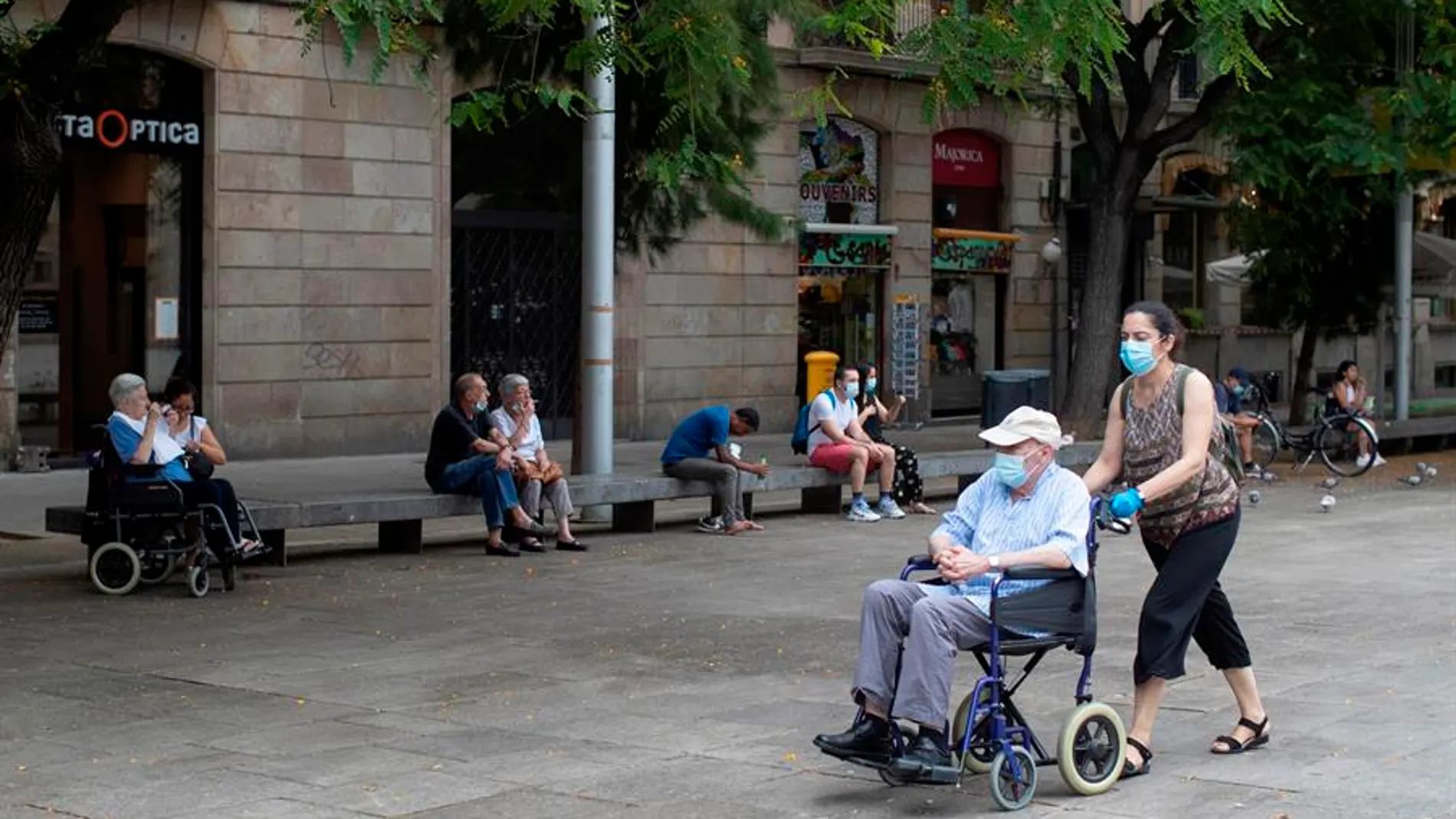 Una mujer empuja la silla de un señor mayor en el centro de Barcelona.