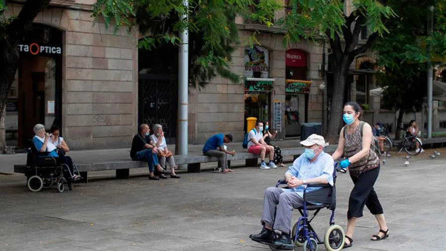 Una mujer empuja la silla de un señor mayor en el centro de Barcelona.