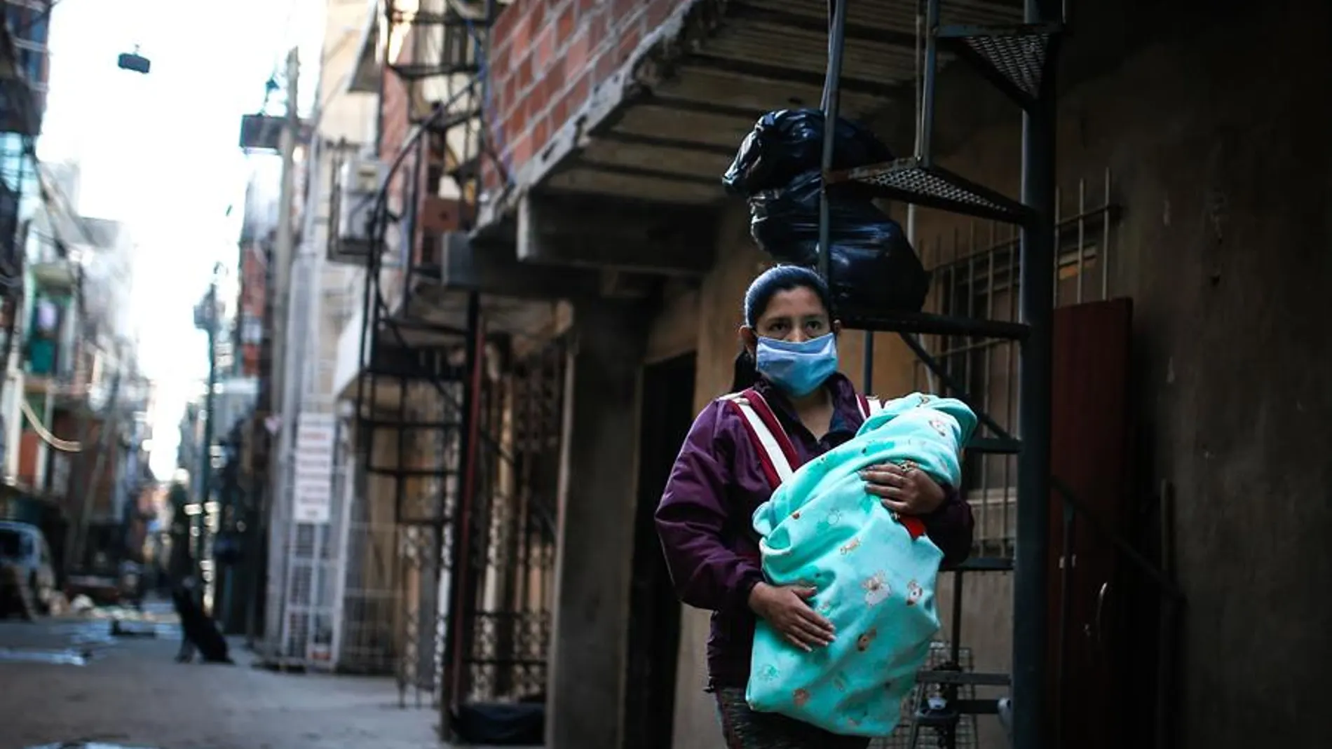 Una mujer con mascarilla lleva a su bebé por una calle de la Villa 31, Buenos Aires
