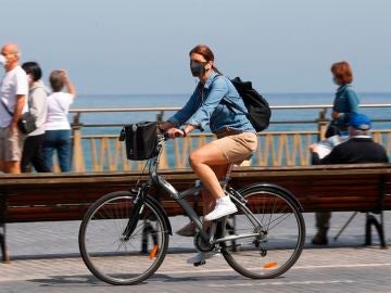 Una mujer pasea en bicicleta protegida con una mascarilla por el paseo de la Zurriola de San Sebastián