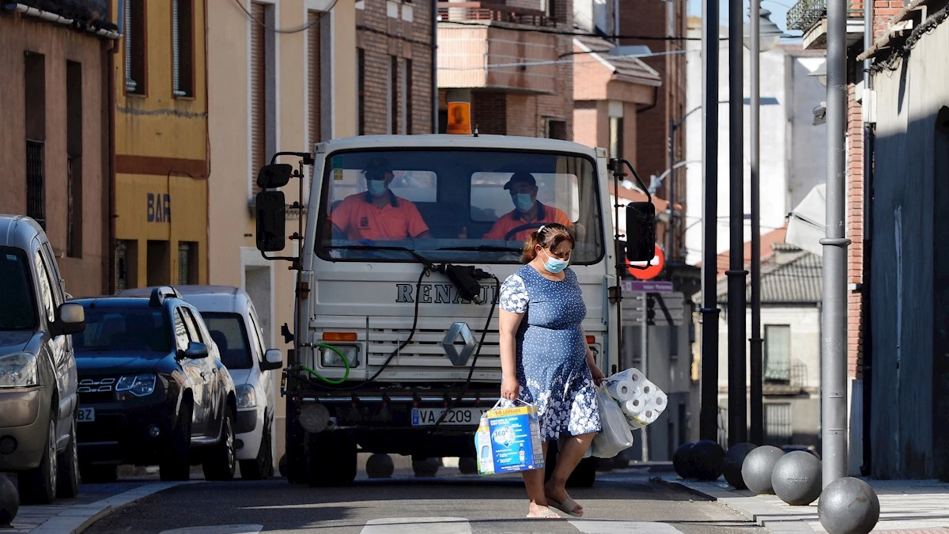  Una mujer pasa por delante de un camión que realiza tareas de desinfección por las calles de Íscar