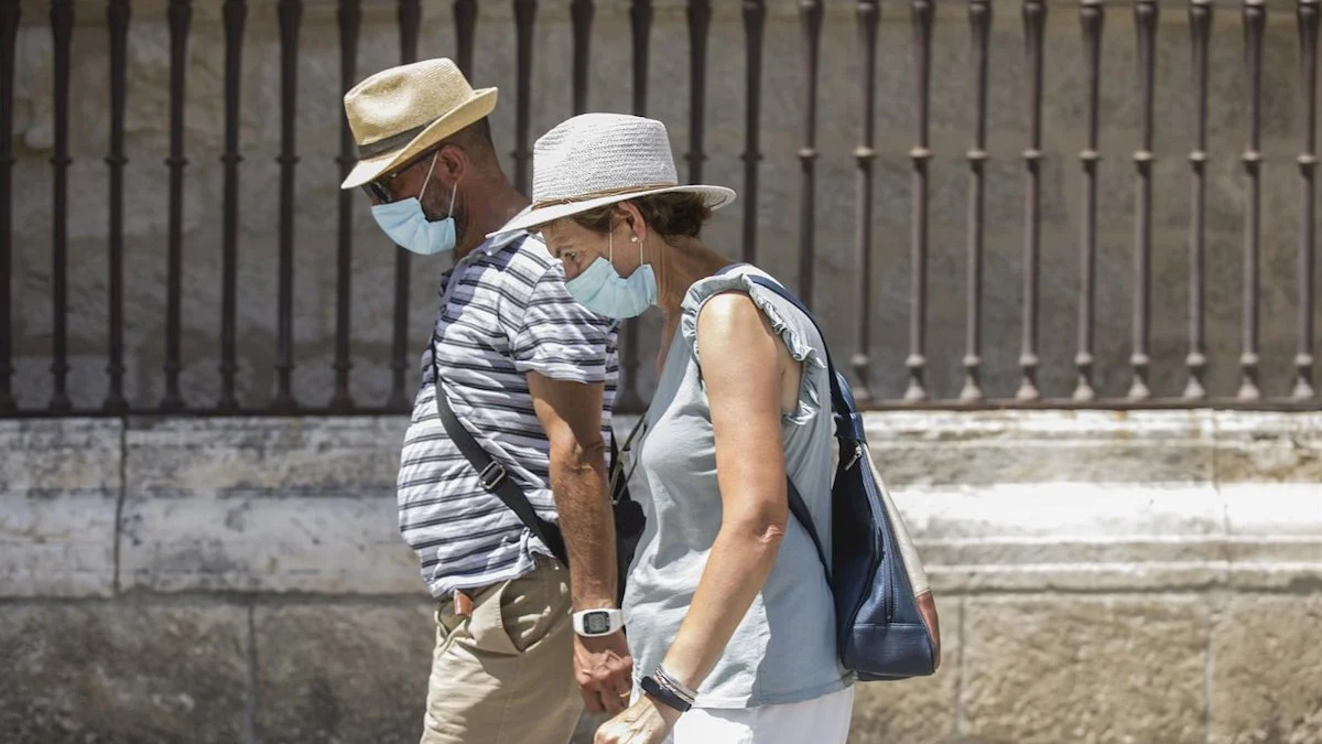 Dos personas caminan con mascarilla y sombrero