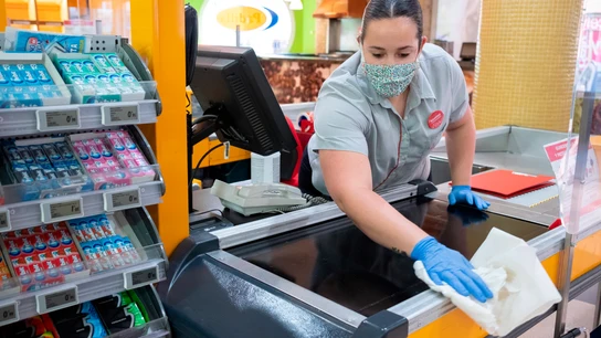 Una empleada de un supermercado desinfecta la caja Una empleada de un supermercado desinfecta la caja