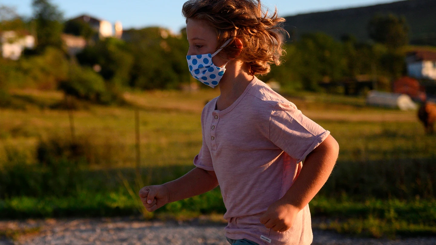 Un niño con mascarilla juega en la calle Un niño con mascarilla juega en la calle