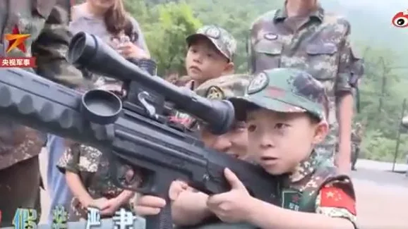 Un niño chino sostiene un arma durante una visita a un centro de entrenamiento militar