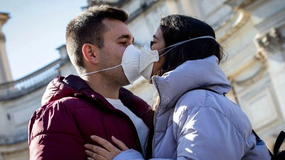 Dos jóvenes besándose con mascarilla