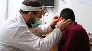 Un médico ausculta el oído de un paciente.