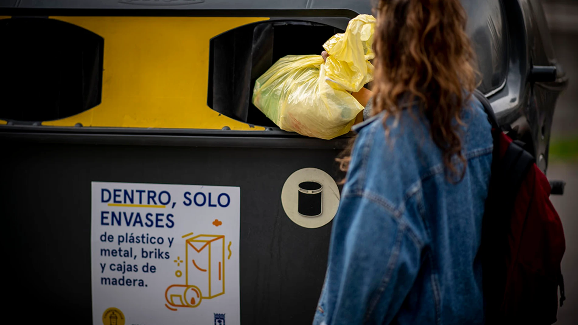 Una mujer tira una bolsa de basura al contenedor amarillo