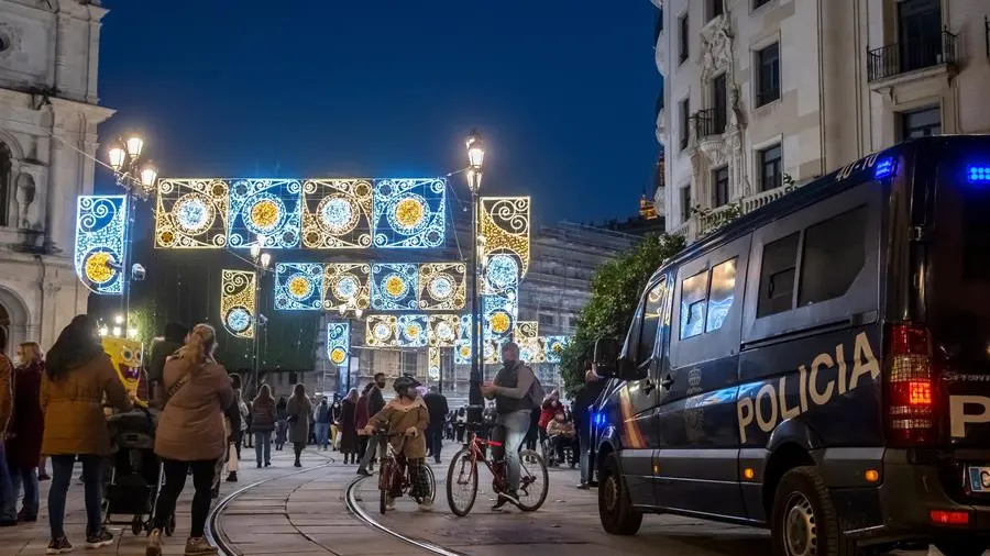 Varias personas caminan por una calle iluminada con motivo de la Navidad en Sevilla.