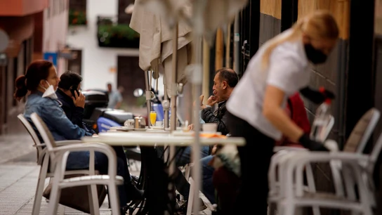 Una camarera de una cafetería de Santa Cruz de Tenerife limpia una mesa mientras varios clientes consumen en la terraza Una camarera de una cafetería de Santa Cruz de Tenerife limpia una mesa mientras varios clientes consumen en la terraza